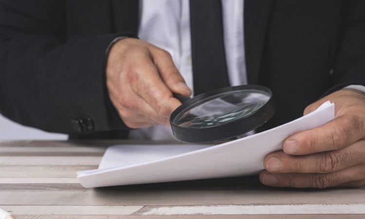 Close-up of the hands of a Businessman looking through a magnifying glass for documents